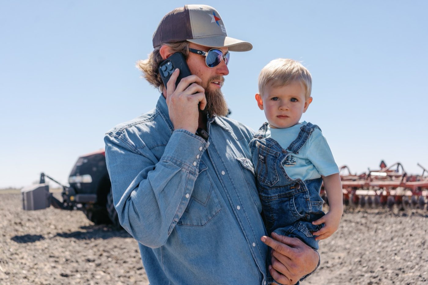 A farmer holding his young son at the edge of a plowed field