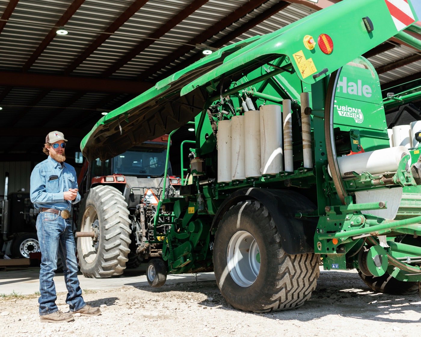 A producer standing beside a hay baler in an equipment barn