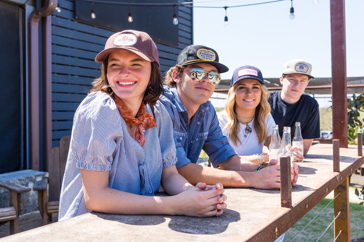 Four people in branded caps around an outdoor table at a ranch venue